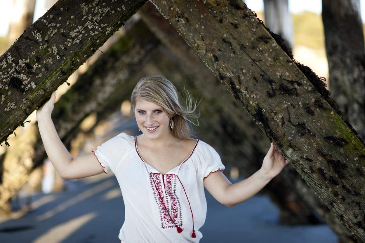Senior portrait of a young woman with arms raised standing under a tree tunnel over a path