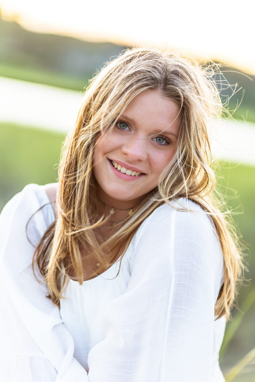 Senior portrait of a young woman with wavy hair smiling outdoors in a white top