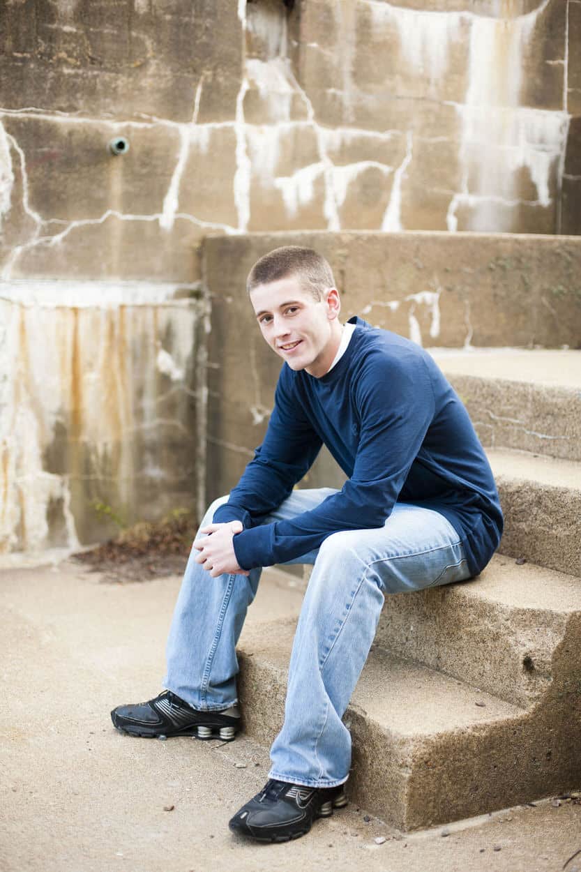 Senior portrait of a young man in a blue sweater sitting on outdoor stone steps