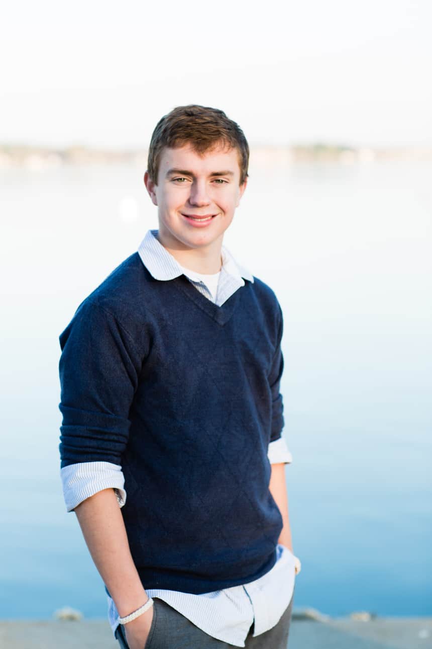 Senior portrait of a young man in a navy sweater standing by a lake