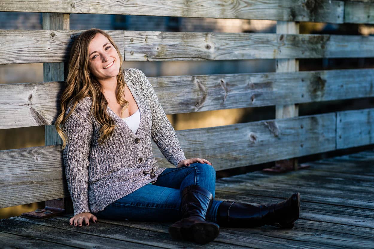 Senior portrait of a young woman in a gray cardigan sitting on a wooden dock