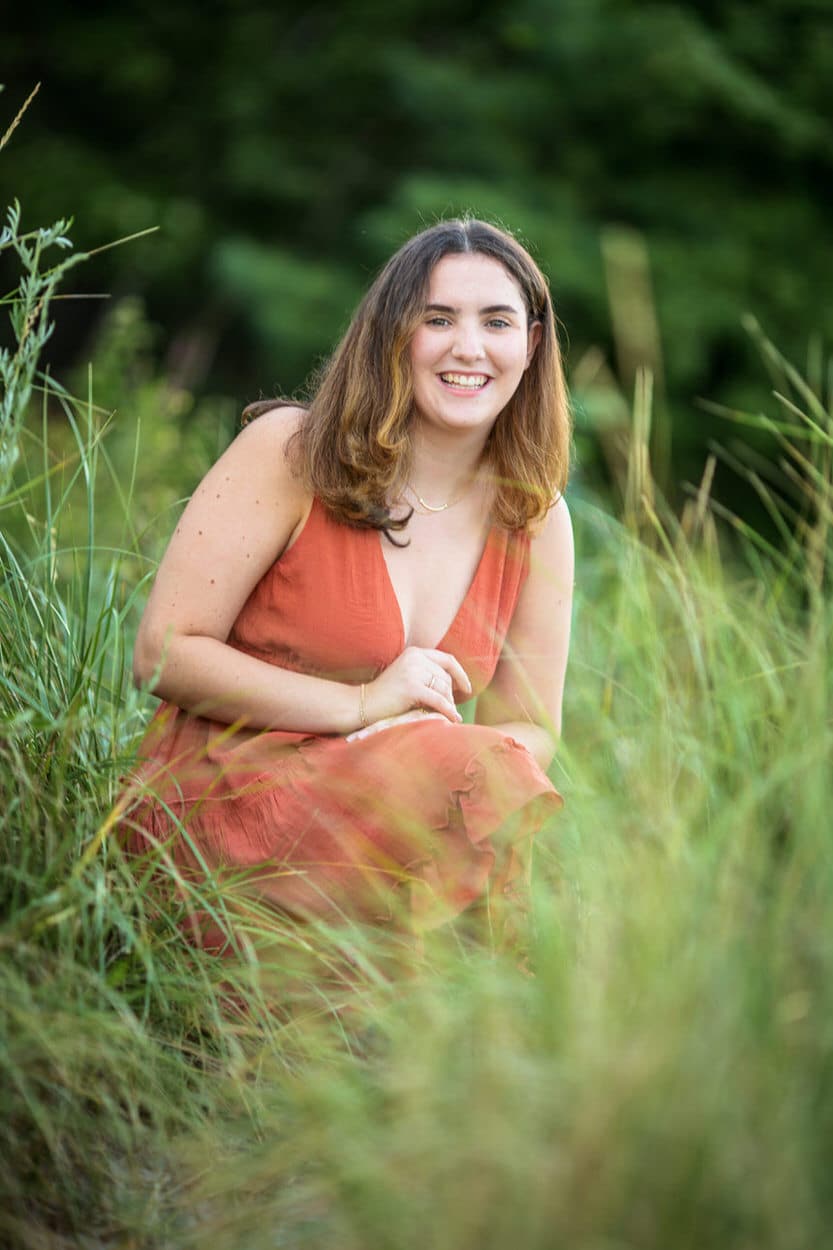 Senior portrait of a young woman in an orange dress sitting in tall grass