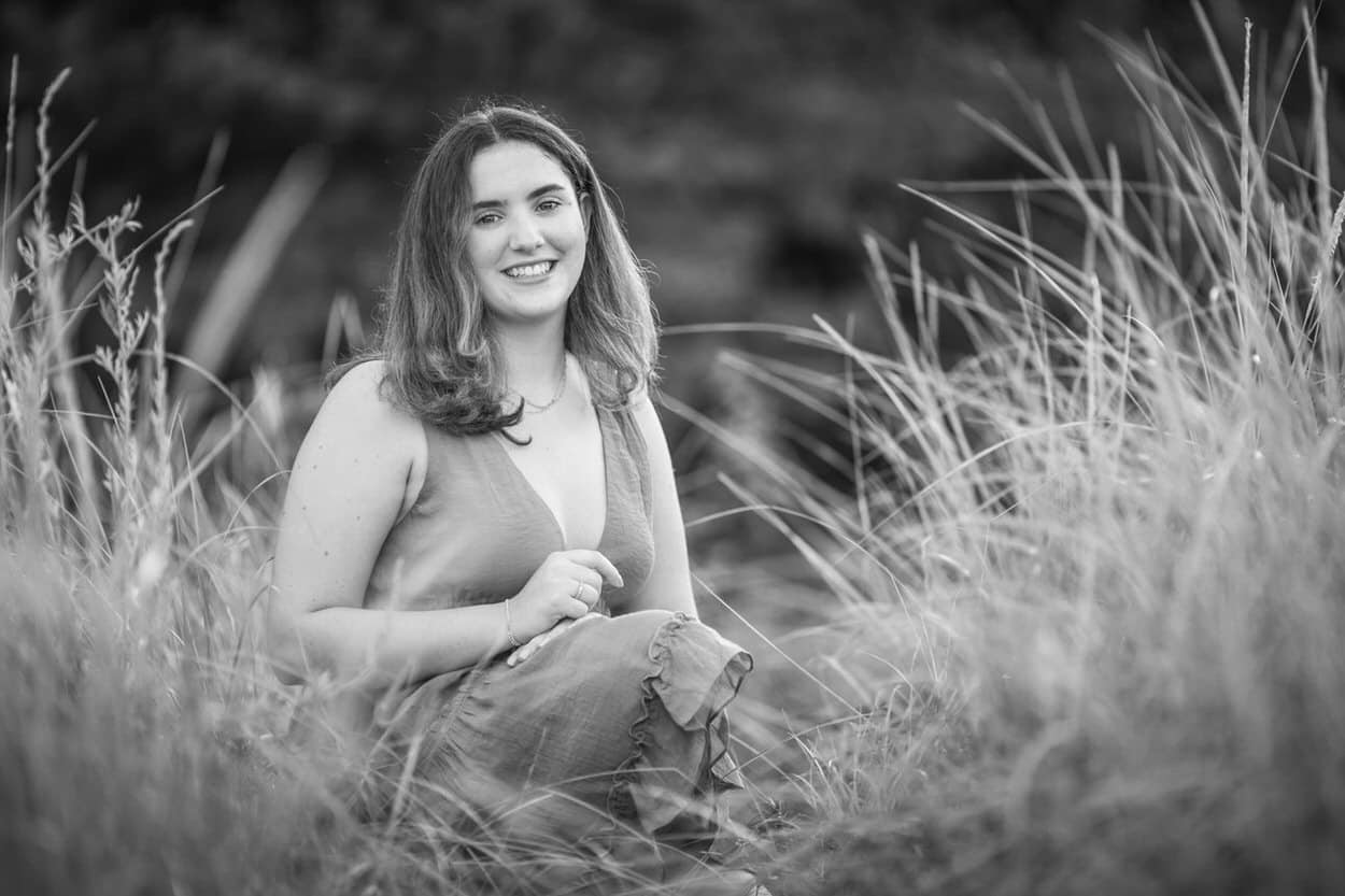 Black and white senior portrait of a young woman sitting in tall grass