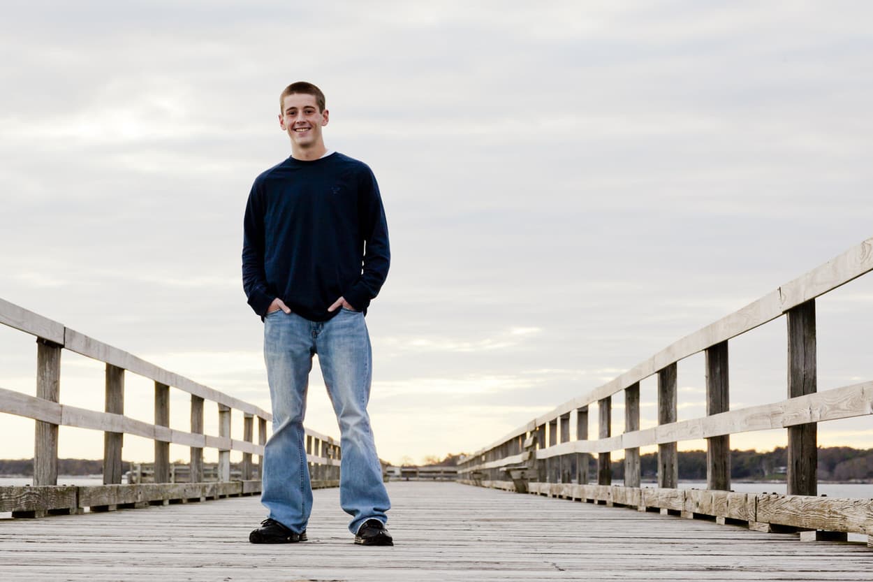 Senior portrait of a young man standing on a long wooden pier