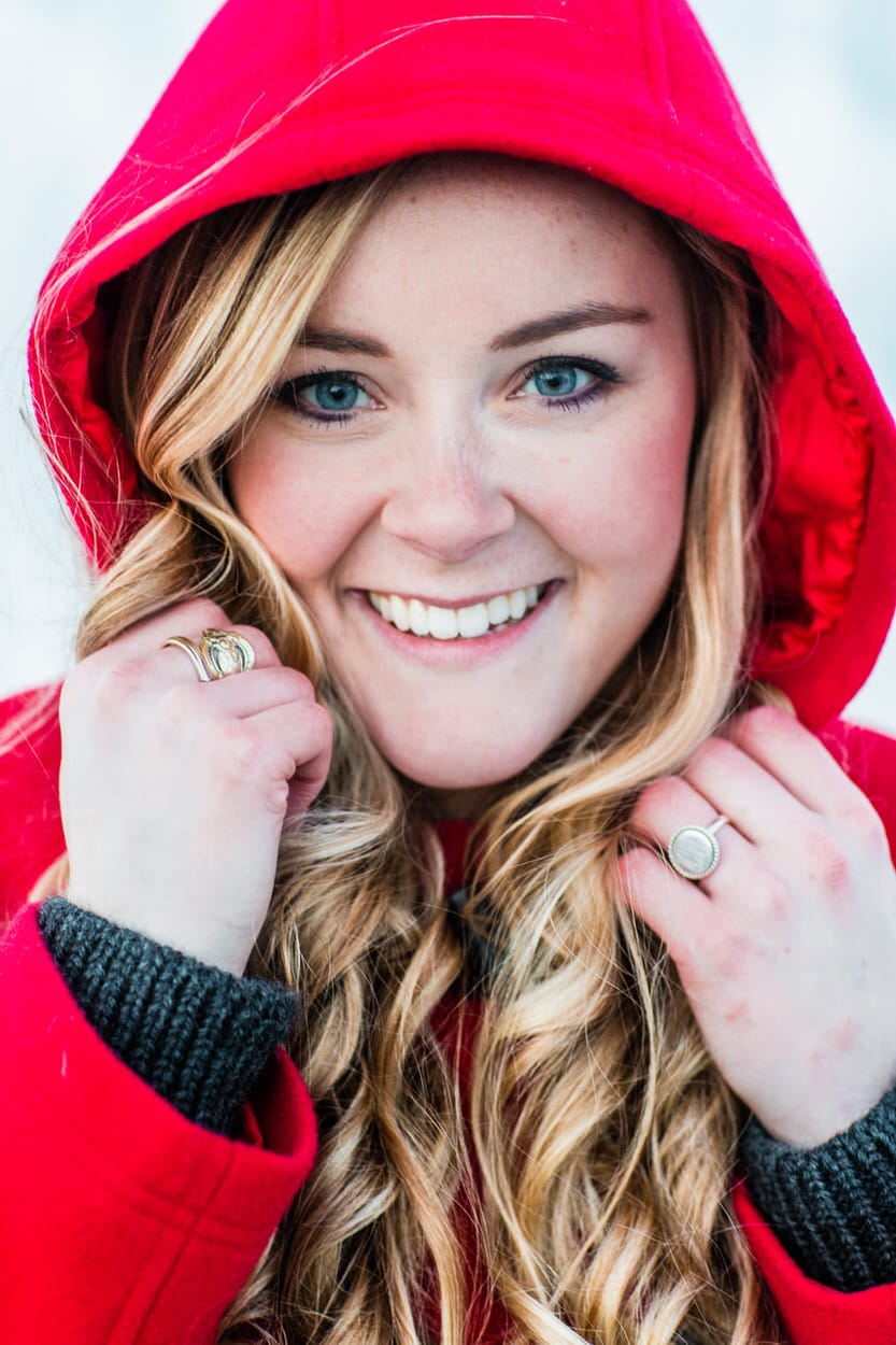 Close-up senior portrait of a young woman in a red hooded jacket smiling
