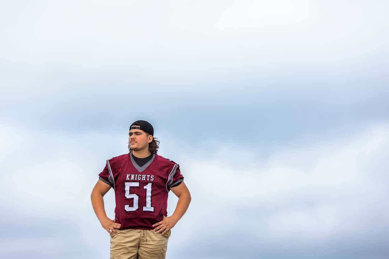 Senior portrait of a young man in a maroon football jersey standing on a track