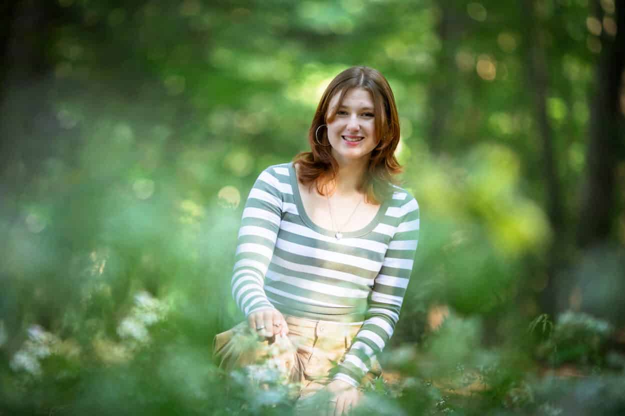 Senior portrait of a young woman in a striped sweater standing among trees