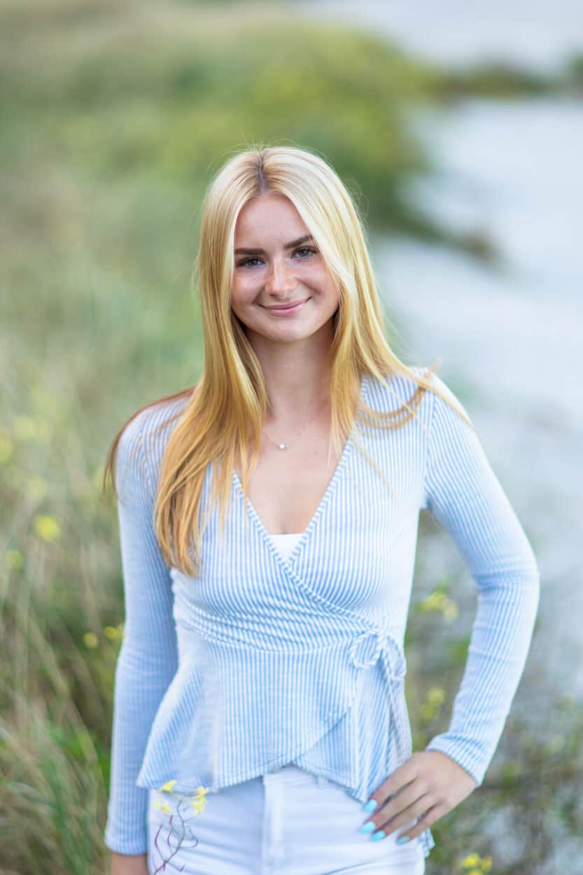 Senior portrait of a young woman in a white knit top standing in tall dune grass
