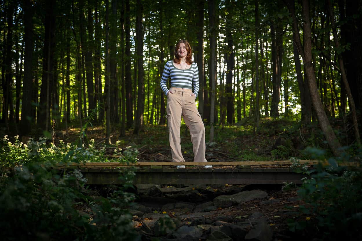 Senior portrait of a young man standing on a log in a forest