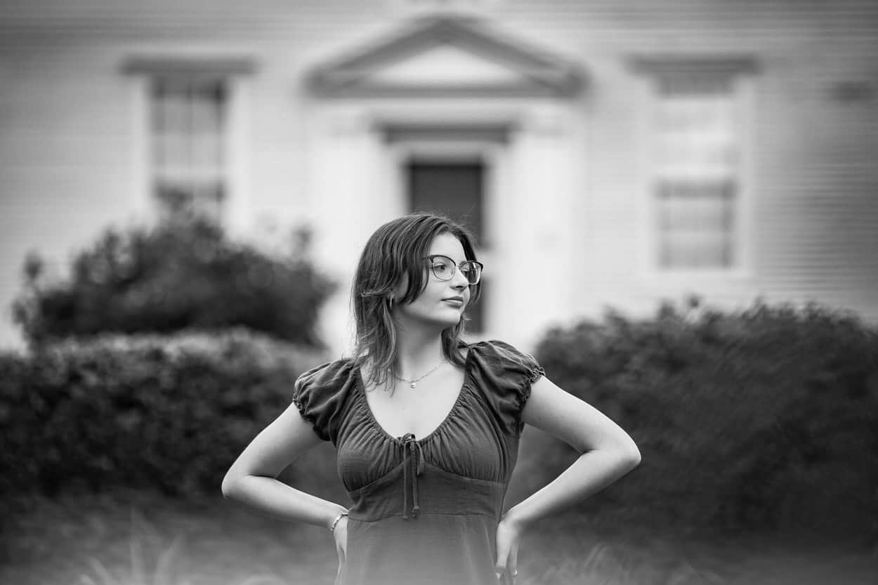 Black and white senior portrait of a young woman standing in front of a building, hand on hip