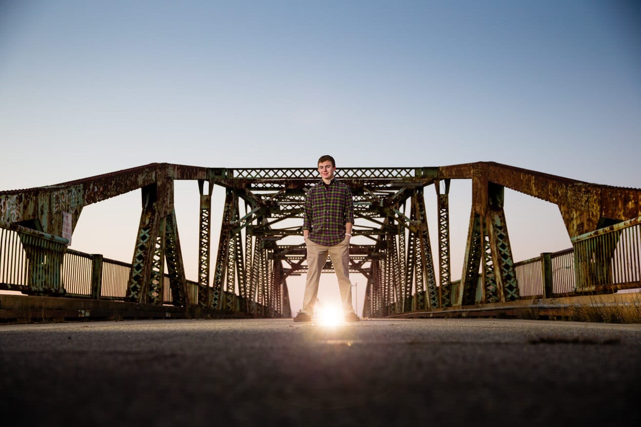 Senior portrait of a young man standing on a railroad trestle bridge at sunset