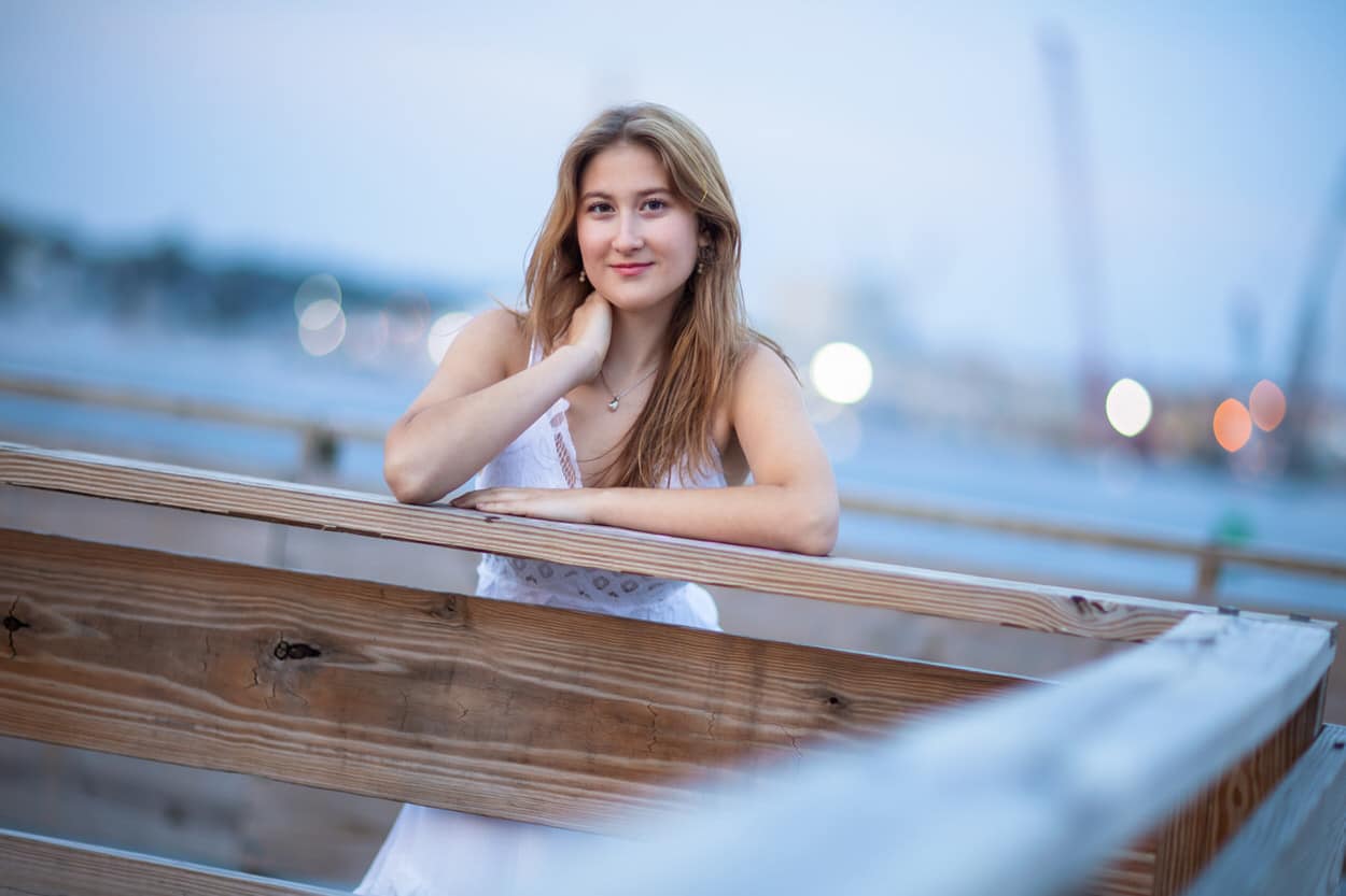 Senior portrait of a young woman leaning on the side of a wooden boat with a city skyline in the background