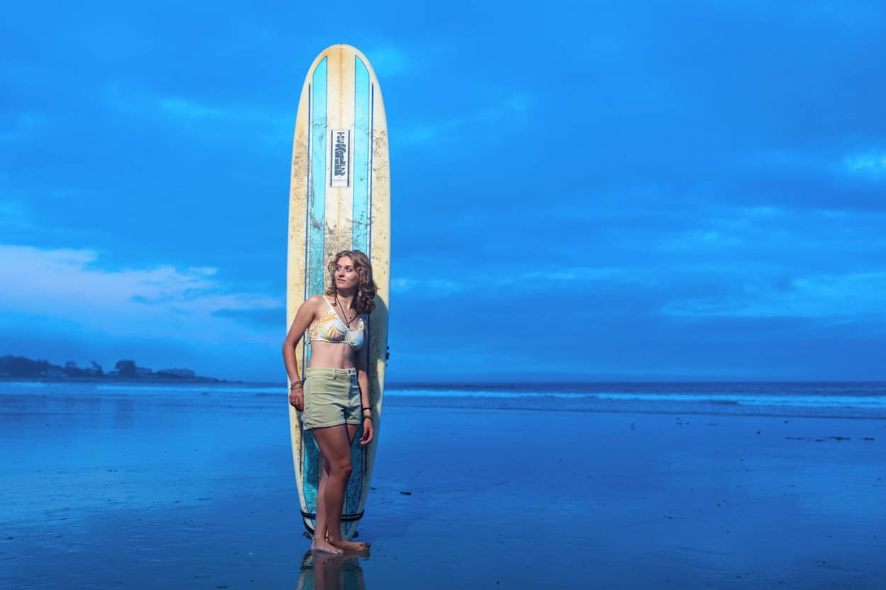 Senior portrait of a young woman standing on a paddleboard in calm water at dusk