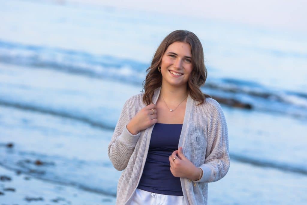 Senior portrait of a young woman in a denim jacket standing on a beach