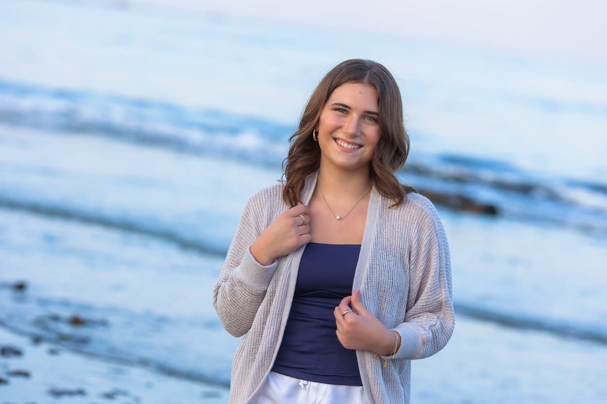 Senior portrait of a young woman in a denim jacket standing on a beach