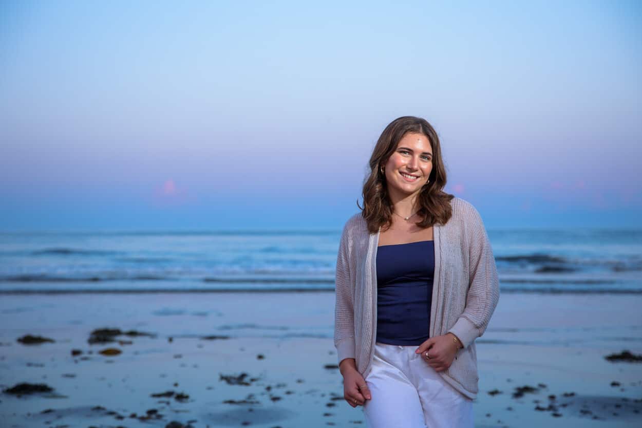 Senior portrait of a young woman in a cardigan smiling on a beach at dusk