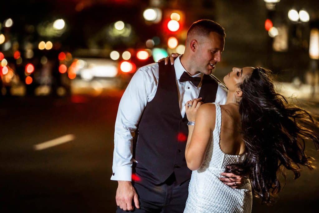 Bride and groom dancing closely on a city street at night with traffic lights blurred behind them
