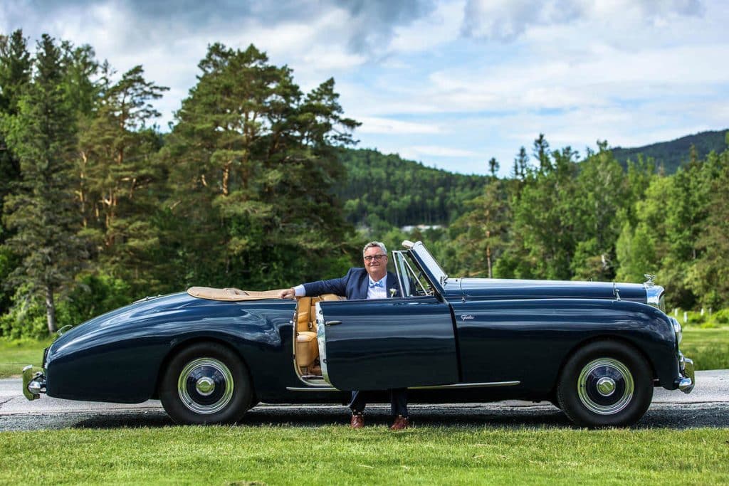Vintage dark blue convertible car parked on a lawn with two people inside