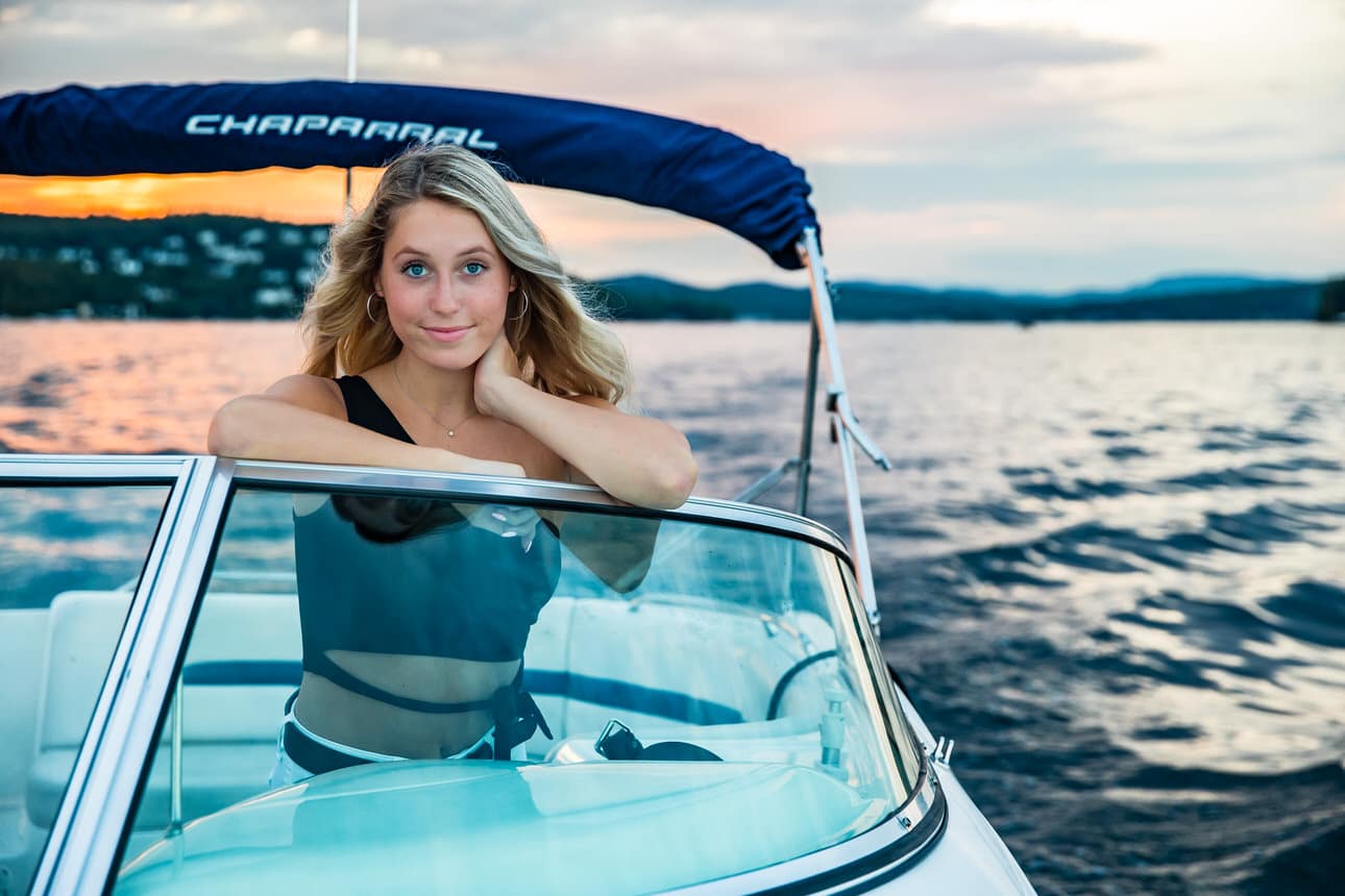Senior portrait of a young woman sitting on a boat at sunset, wearing a swimsuit
