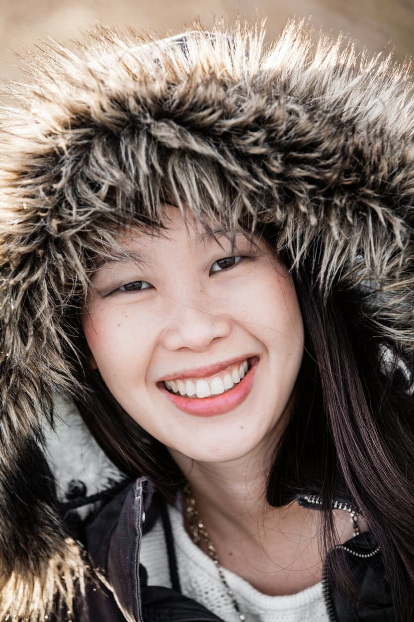 Close-up senior portrait of a young woman in a fur-hooded winter jacket smiling broadly