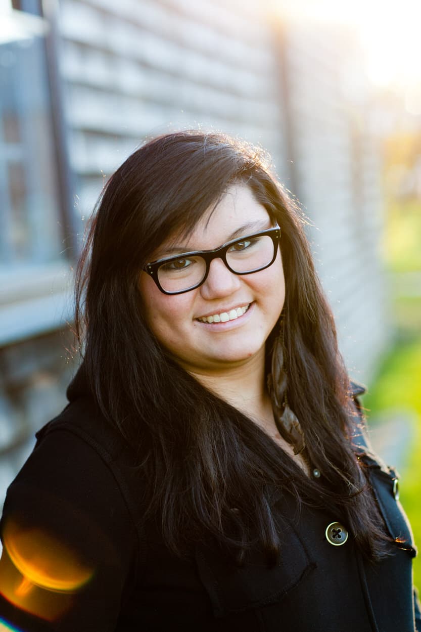 Close-up senior portrait of a young woman with glasses smiling in a black top