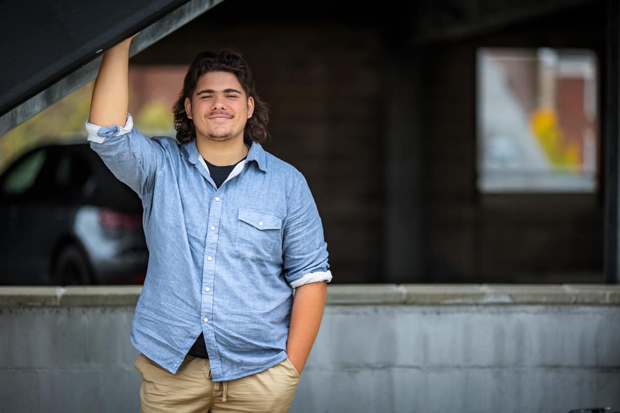 Senior portrait of a young man leaning against a porch column