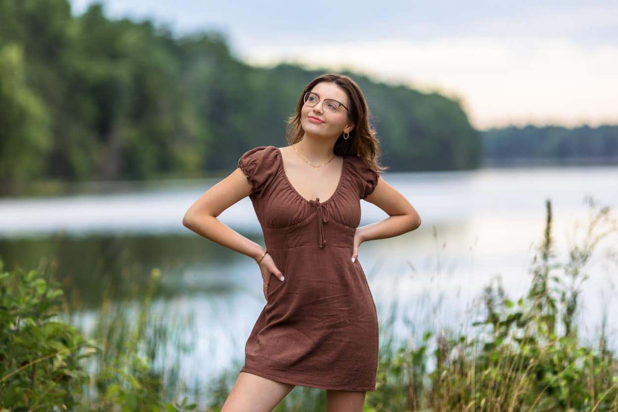Senior portrait of a young woman in a brown dress standing by a lake