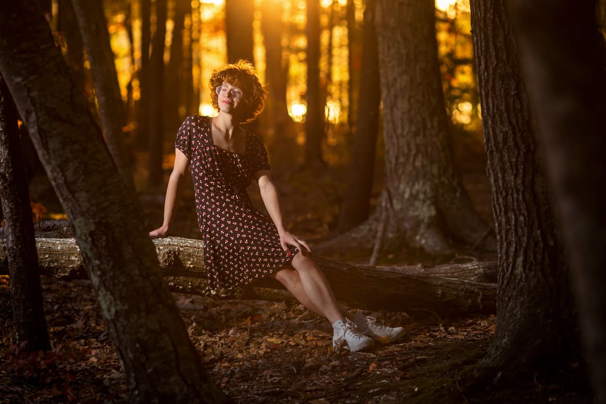 Senior portrait of a young woman in a floral dress sitting on a log in a sunlit forest