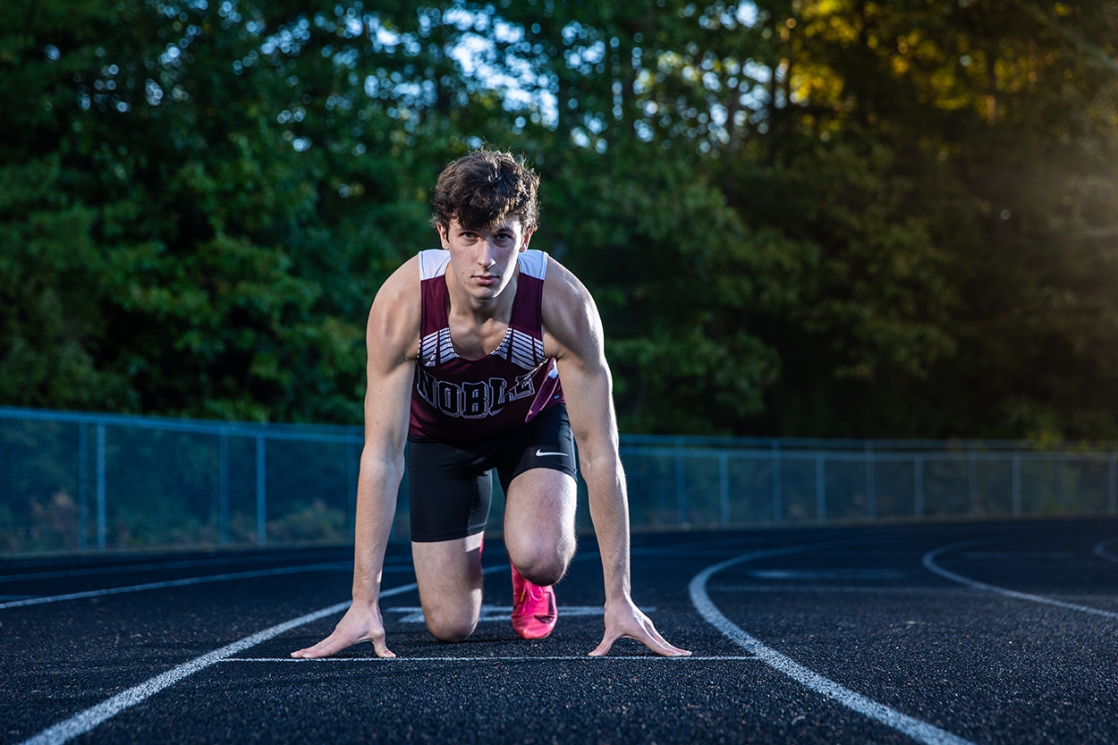 Senior portrait of a young man in athletic gear in a track starting position on a running track