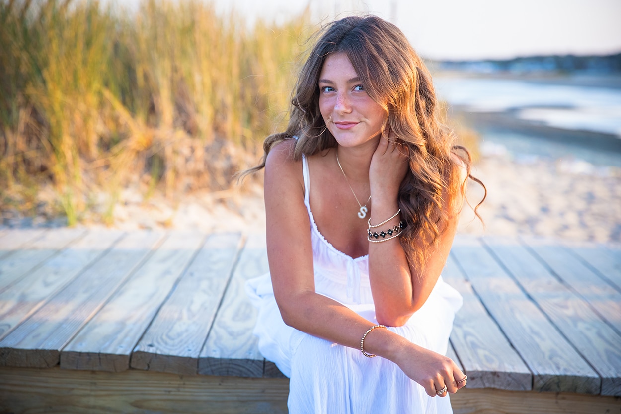 Senior portrait of a young woman in a striped outfit standing on a beach with the tide reflecting the sky