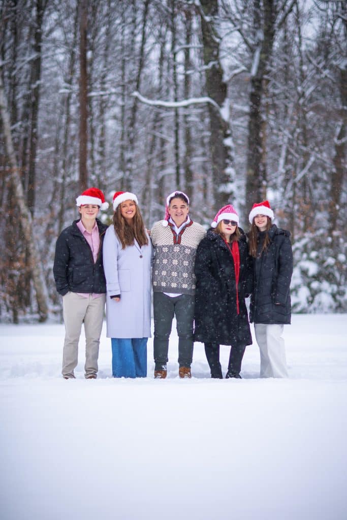 Family in Santa hats standing together in a snowy forest for a holiday portrait